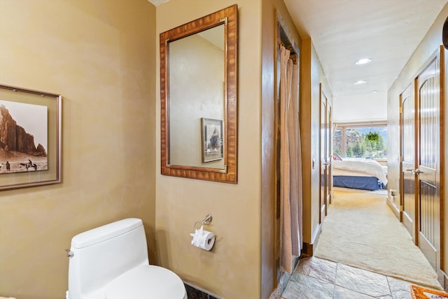 ensuite bathroom with toilet, stone finish floor, recessed lighting, baseboards, and ensuite bathroom