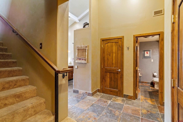 staircase with beam ceiling, high vaulted ceiling, baseboards, visible vents, and stone tile flooring