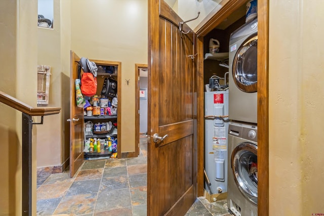 washroom featuring stone tile flooring, laundry area, water heater, and stacked washer / drying machine