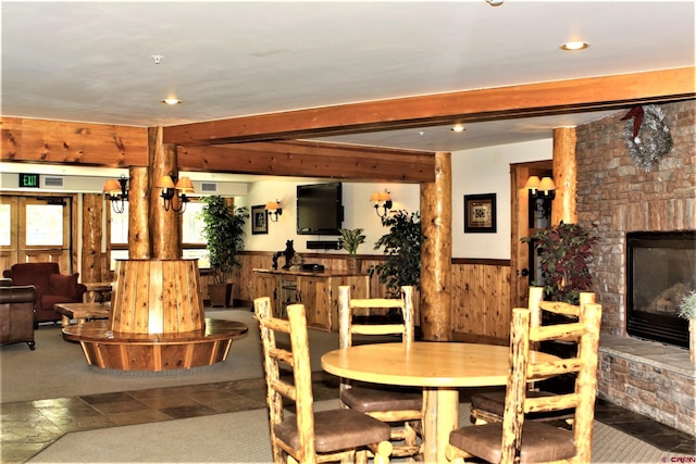 dining room featuring a fireplace, wood walls, a wainscoted wall, beamed ceiling, and visible vents