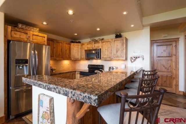 kitchen featuring appliances with stainless steel finishes, a kitchen breakfast bar, recessed lighting, and dark stone countertops