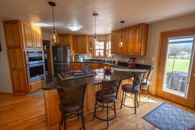kitchen with hanging light fixtures, appliances with stainless steel finishes, a breakfast bar area, brown cabinetry, and light wood-style flooring
