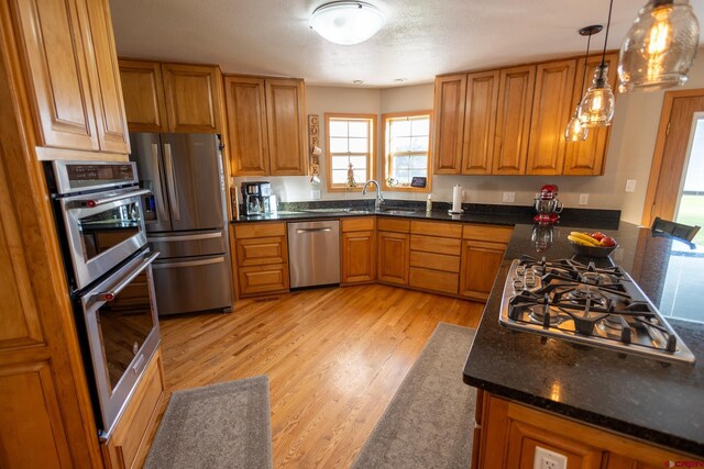 kitchen with pendant lighting, appliances with stainless steel finishes, light wood-type flooring, brown cabinets, and a sink