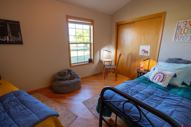 bedroom featuring baseboards, wood finished floors, lofted ceiling, and a closet
