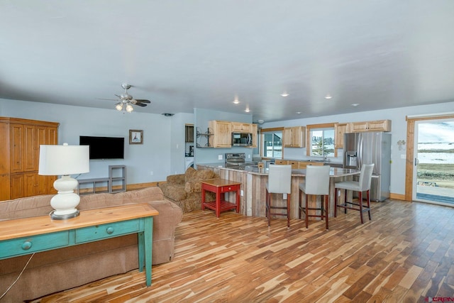living room featuring light wood-style floors, a ceiling fan, and baseboards