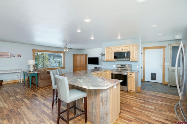 kitchen with light wood-type flooring, appliances with stainless steel finishes, light brown cabinets, and a breakfast bar