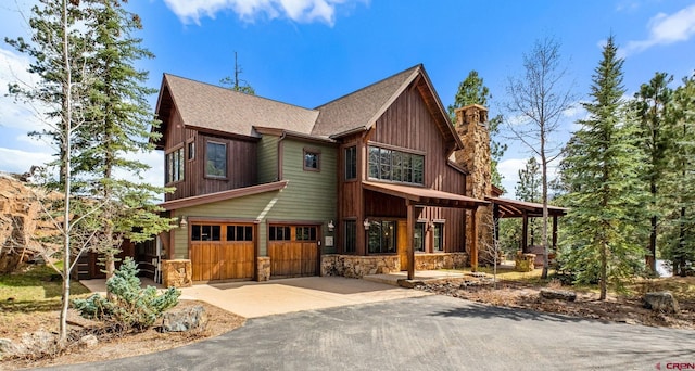 chalet / cabin with a shingled roof, stone siding, a garage, a chimney, and driveway