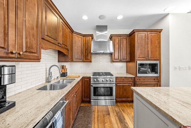 kitchen featuring dark wood-style flooring, light stone countertops, a sink, wall chimney exhaust hood, and stainless steel appliances