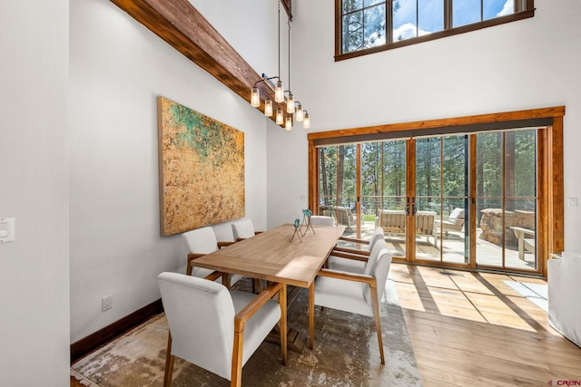 dining space with baseboards, hardwood / wood-style flooring, and a towering ceiling