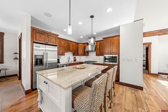 kitchen with wall chimney range hood, backsplash, baseboards, stainless steel appliances, and light wood-style flooring