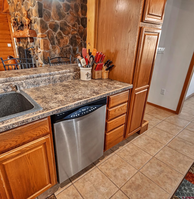 kitchen with stainless steel dishwasher, brown cabinets, light tile patterned floors, baseboards, and a sink