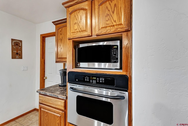 kitchen featuring brown cabinetry, dark countertops, baseboards, appliances with stainless steel finishes, and light tile patterned floors
