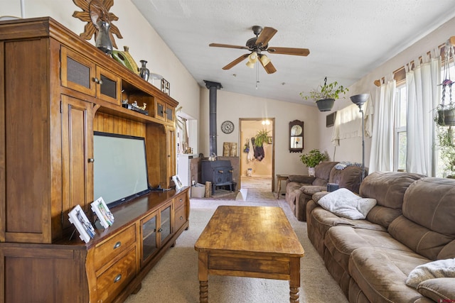 living area with ceiling fan, light carpet, a wood stove, a textured ceiling, and lofted ceiling