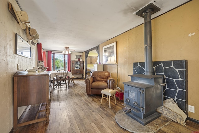 interior space with wood-type flooring, a ceiling fan, a textured wall, and a wood stove