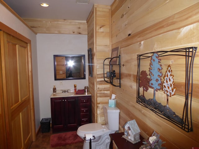 half bath with toilet, wood walls, vanity, and visible vents