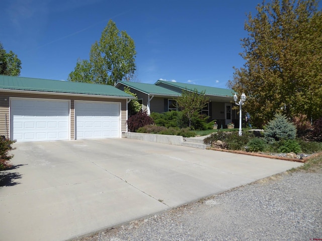ranch-style house with metal roof, an attached garage, and driveway