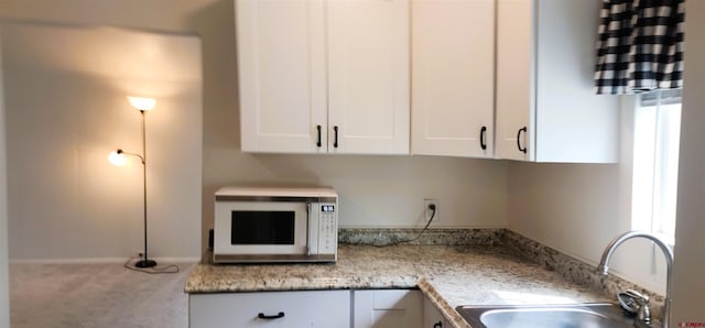 kitchen with a sink, carpet floors, white cabinets, white microwave, and light countertops