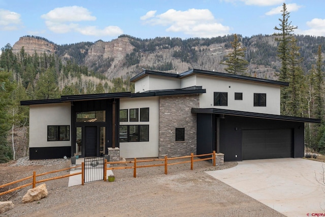 modern home featuring stone siding, a mountain view, a garage, stucco siding, and fence private yard