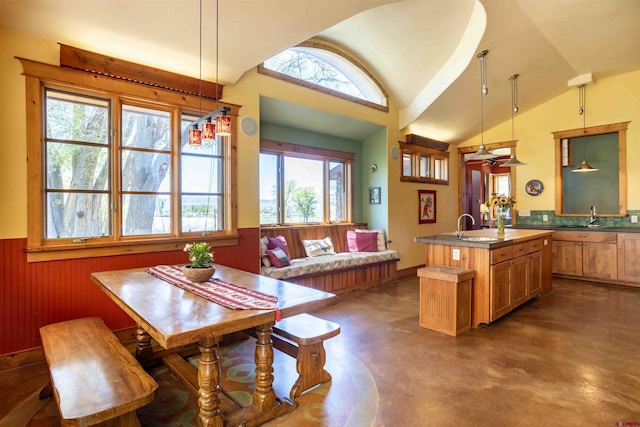 dining room featuring wainscoting, wooden walls, concrete flooring, and lofted ceiling