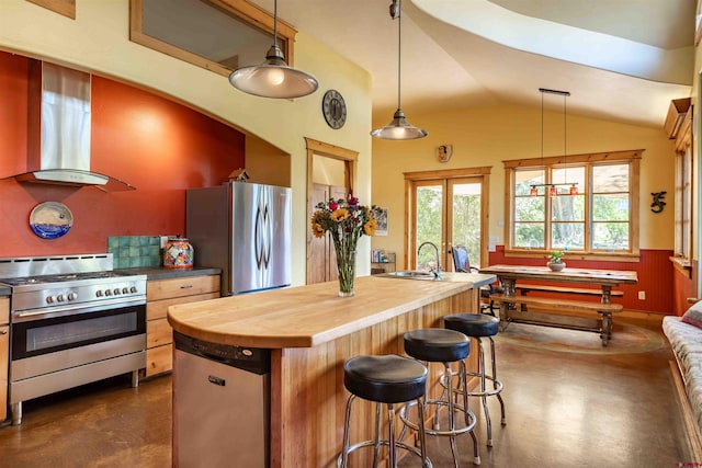 kitchen featuring finished concrete flooring, butcher block counters, a sink, wall chimney exhaust hood, and stainless steel appliances