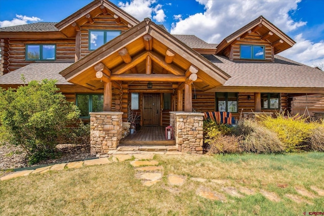 log cabin with log siding, a shingled roof, a front lawn, and covered porch