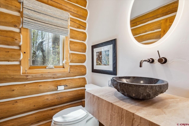 bathroom with toilet, log walls, and a sink