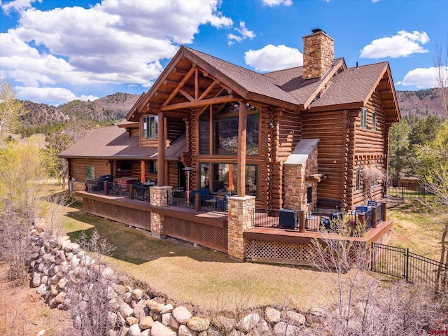 back of house featuring log exterior, fence, a deck with mountain view, and a chimney
