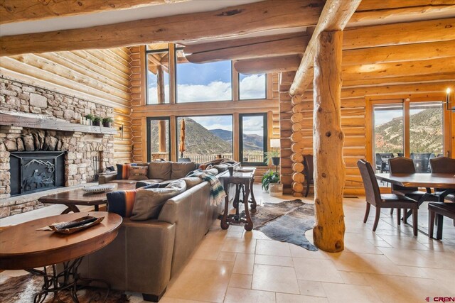 living room with a mountain view, beamed ceiling, a high ceiling, a stone fireplace, and rustic walls