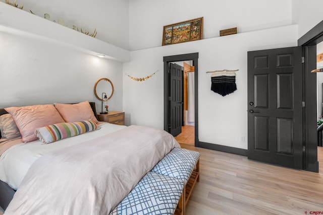 bedroom featuring baseboards, light wood-style floors, and a towering ceiling