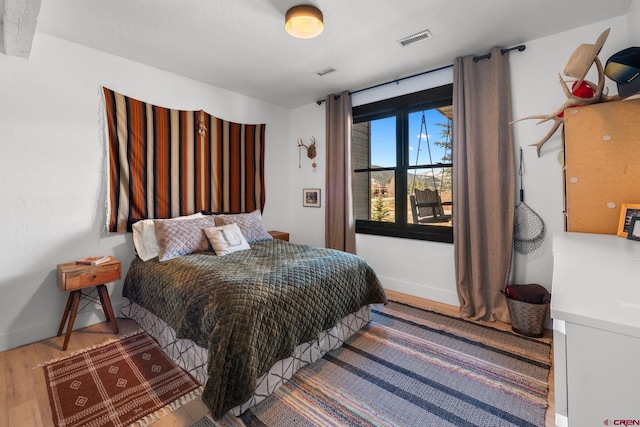 bedroom with baseboards, visible vents, and wood finished floors
