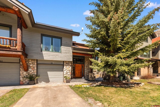 view of front of property featuring a front lawn, driveway, stone siding, and an attached garage