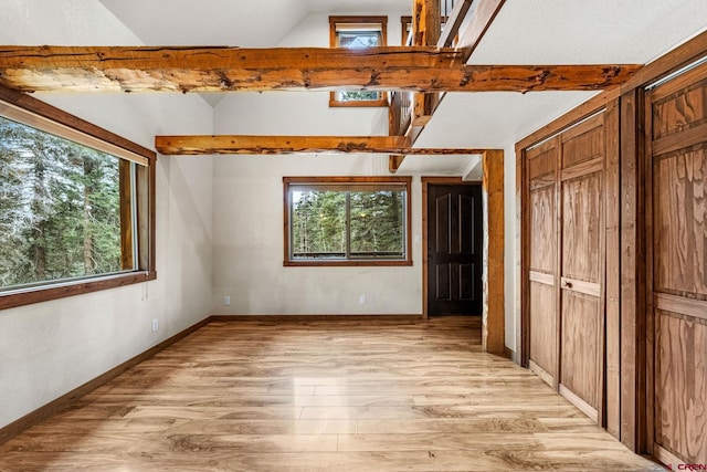 unfurnished bedroom with multiple windows, light wood-style floors, baseboards, and lofted ceiling