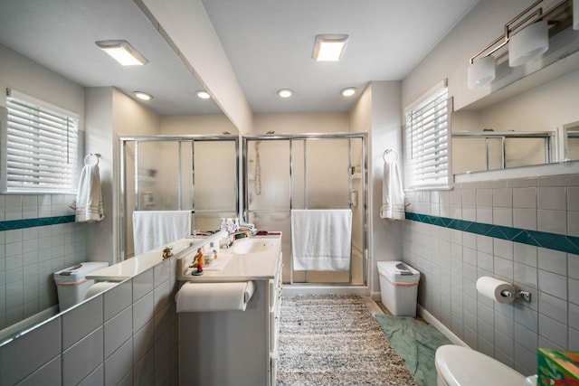 bathroom with tile walls, toilet, a shower stall, vanity, and wainscoting