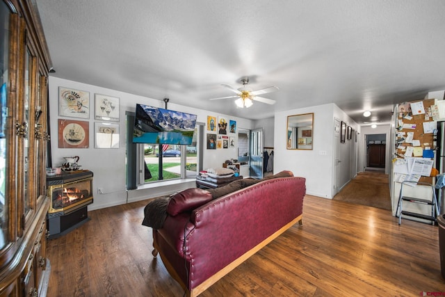 living room with wood finished floors, a wood stove, a textured ceiling, ceiling fan, and baseboards