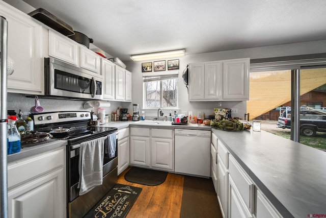 kitchen with appliances with stainless steel finishes, white cabinetry, dark wood-type flooring, a sink, and light countertops