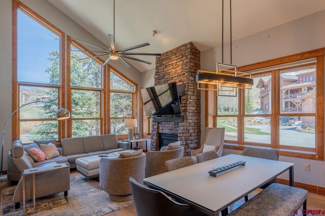 living area with high vaulted ceiling, ceiling fan, a stone fireplace, and wood finished floors