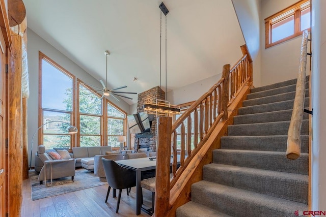 stairway with ceiling fan, a fireplace, hardwood / wood-style floors, and high vaulted ceiling