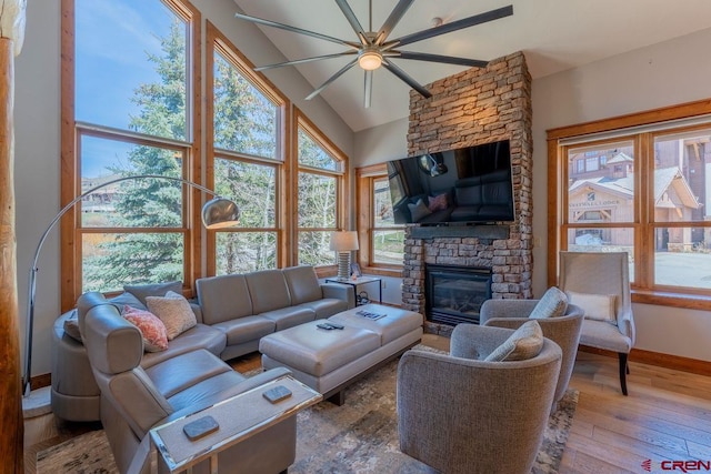 living area with a ceiling fan, a fireplace, hardwood / wood-style floors, baseboards, and vaulted ceiling