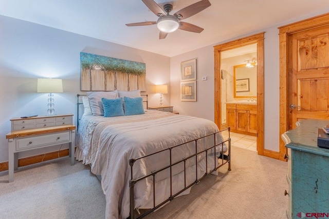 bedroom with baseboards, ensuite bathroom, ceiling fan, a sink, and light colored carpet