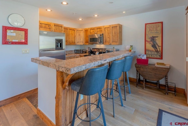 kitchen featuring baseboards, stainless steel appliances, a peninsula, and light wood-type flooring