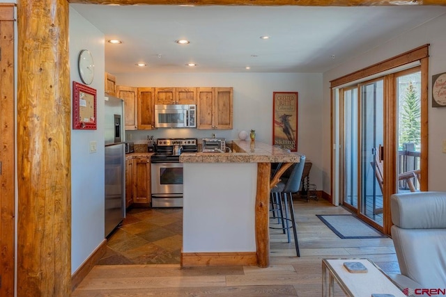 kitchen featuring a peninsula, a breakfast bar area, recessed lighting, baseboards, and appliances with stainless steel finishes