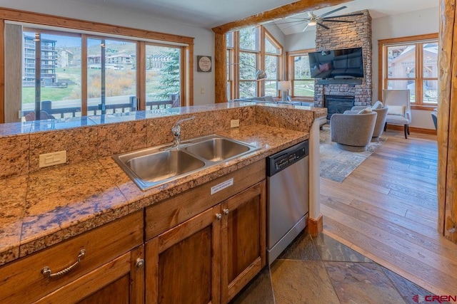 kitchen featuring a sink, brown cabinets, a fireplace, ceiling fan, and stainless steel dishwasher