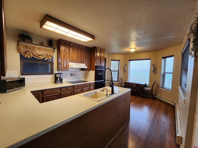 kitchen featuring a sink, dark wood-type flooring, backsplash, black appliances, and light countertops