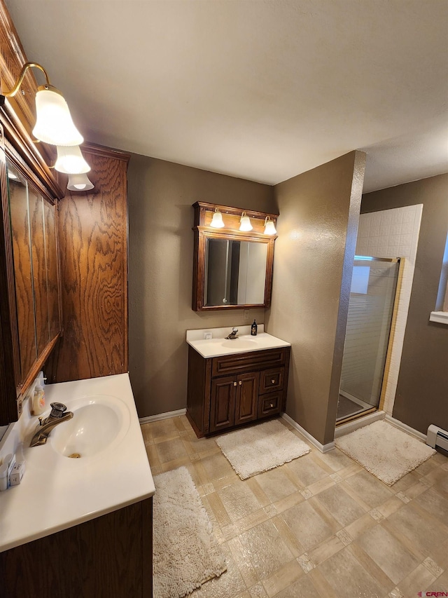 full bath with a sink, two vanities, a stall shower, and baseboards