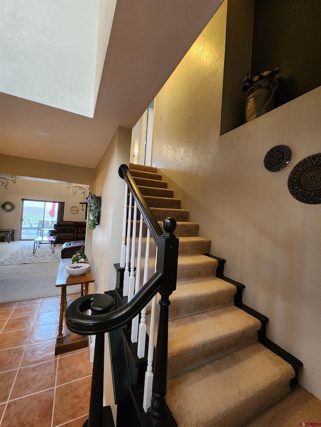 stairway featuring a skylight, a high ceiling, and tile patterned floors