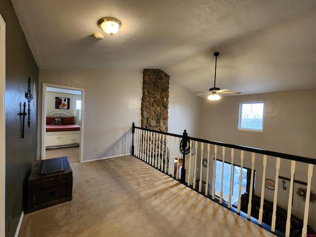 hall featuring an upstairs landing, carpet floors, a textured ceiling, baseboards, and vaulted ceiling