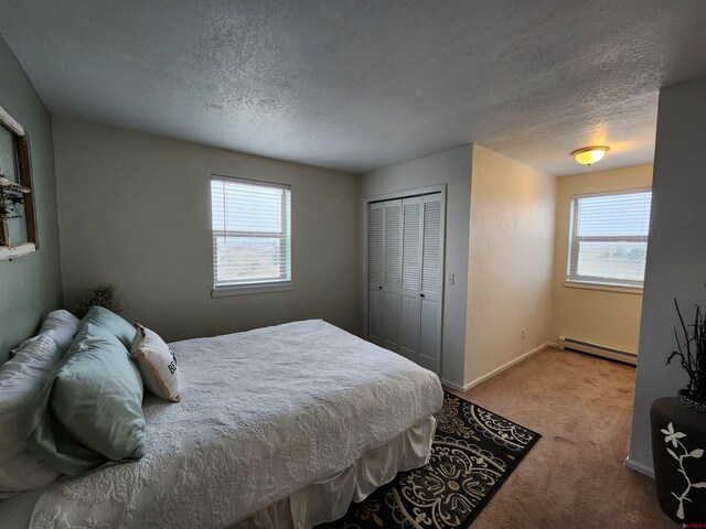 bedroom featuring multiple windows, a textured ceiling, a baseboard radiator, and carpet floors
