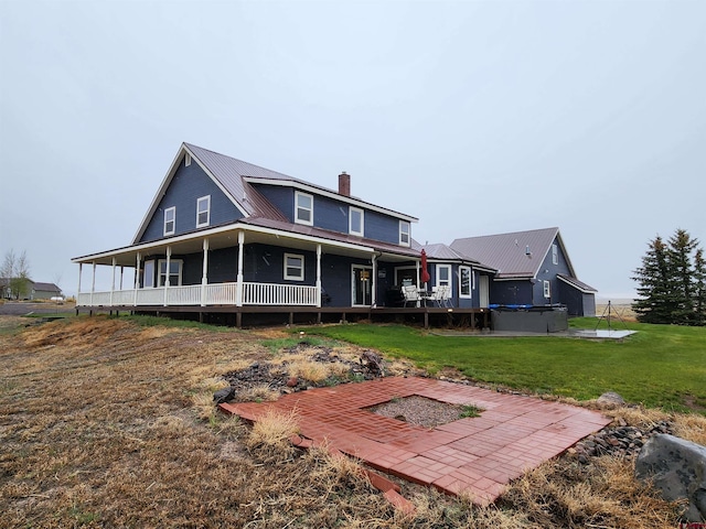 rear view of house featuring metal roof, covered porch, a chimney, and a lawn