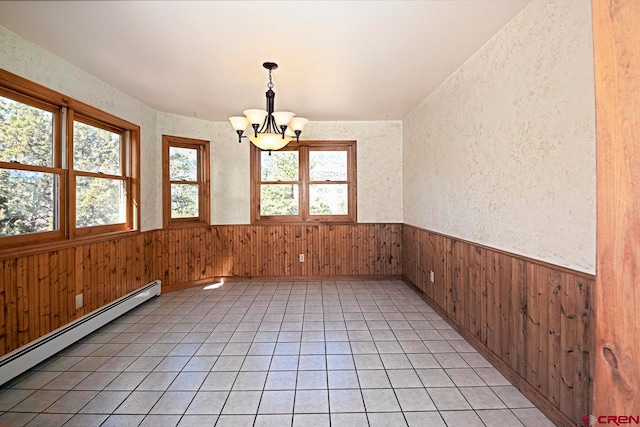 empty room featuring a baseboard heating unit, an inviting chandelier, wainscoting, and wood walls