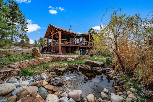 back of property featuring a small pond, a wooden deck, and stairway